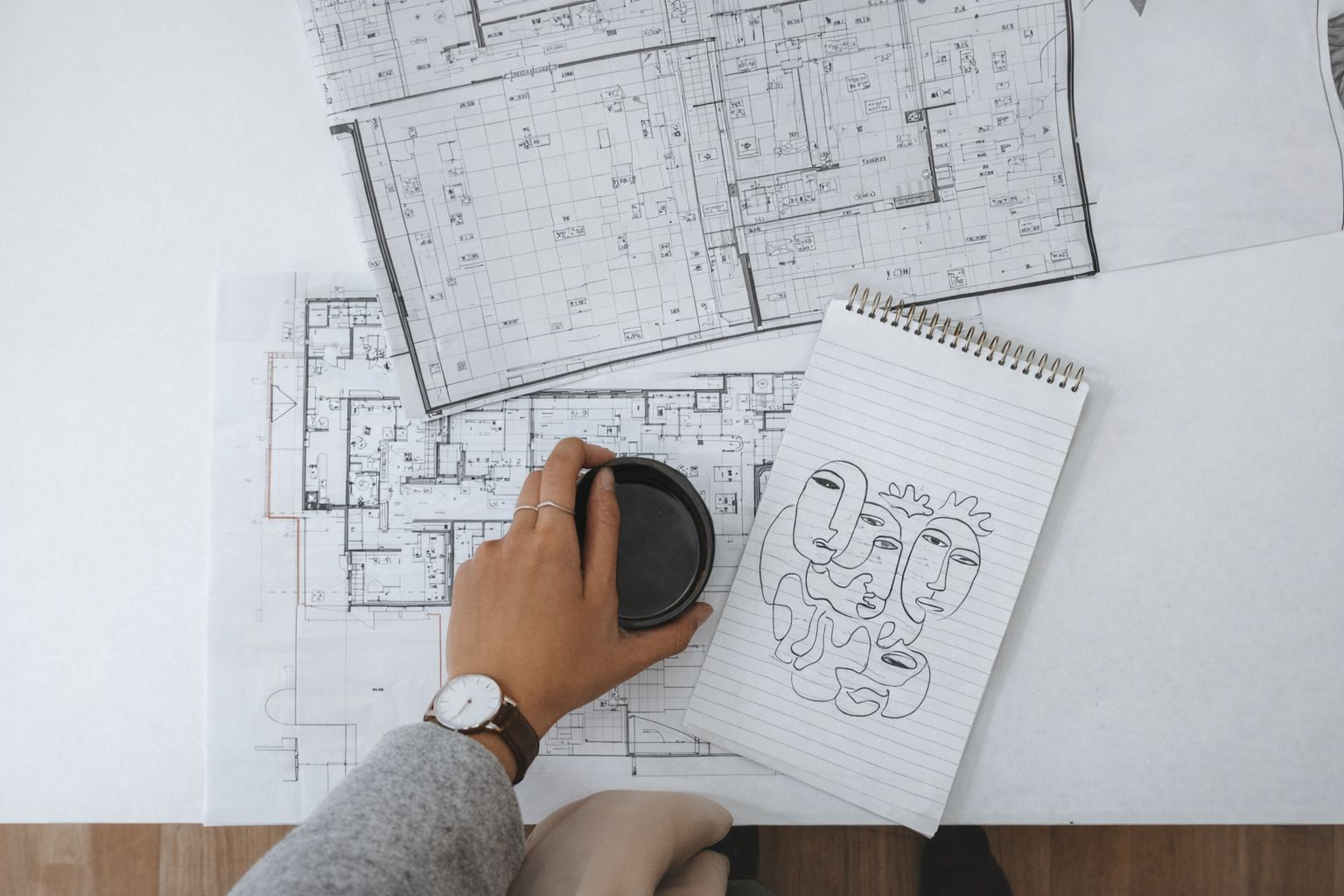 Arkitekttegninger på et bord med en kaffekopp og skisseblokk.